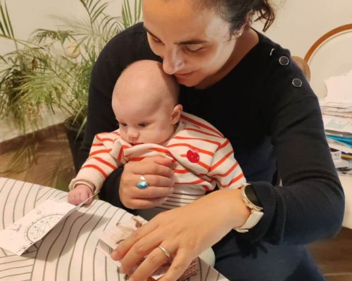 Photo d'une maman avec un bébé dans les bras qui découvre un carnet Astro Baby.